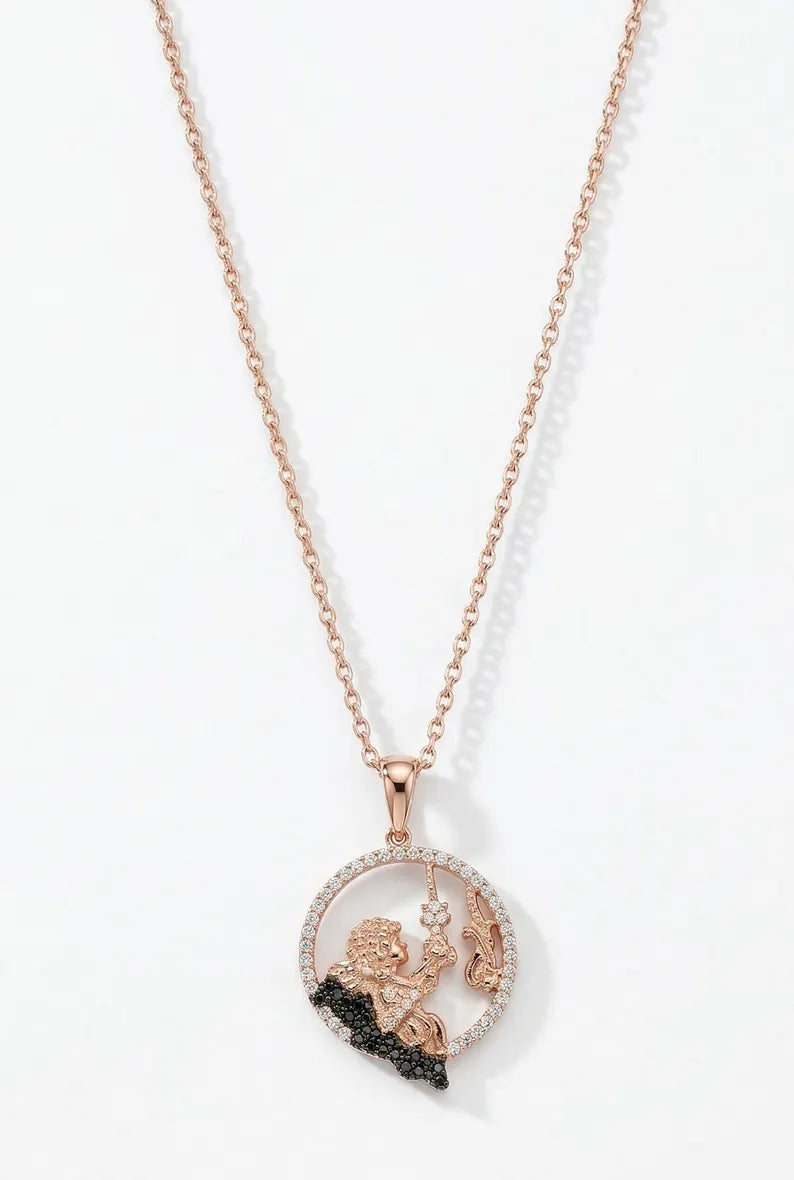 A rose gold pendant necklace featuring a circular design with a small cherub figure, a halo of clear stones, and a black textured accent at the bottom, displayed on a clean white background.