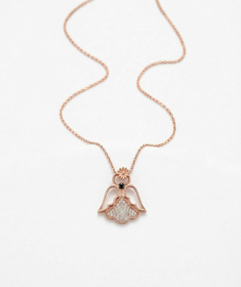A rose gold angel pendant necklace with a small black eye detail and clear pavé accents, shown on a delicate chain against a clean white background.