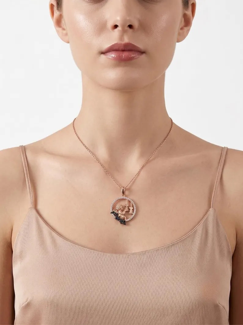 A close-up of a model wearing a rose gold pendant necklace with a circular design and a small dark blue floral accent, paired with a beige camisole top against a light gray background.
