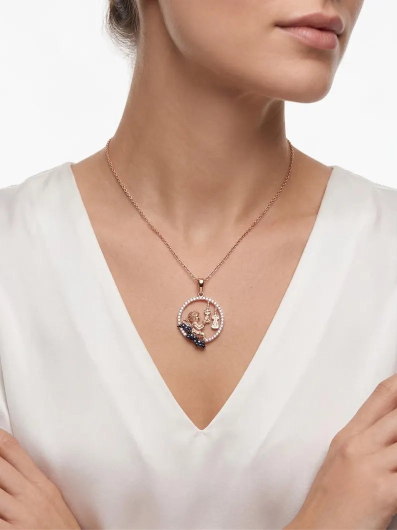 A close-up of a woman wearing a delicate rose gold necklace with a circular pendant featuring a central figure and dark blue accents, paired with a white V-neck top.