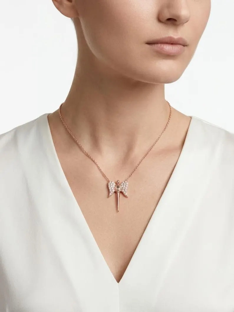 A close-up of a model wearing a delicate rose gold necklace with a bow-shaped pendant adorned with small sparkling crystals, paired with a white V-neck top.