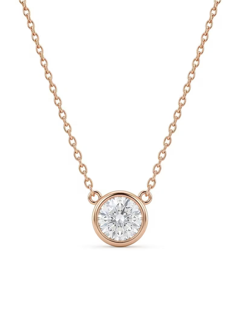 A delicate rose gold chain necklace featuring a round bezel-set clear gemstone pendant, shown against a solid white background.