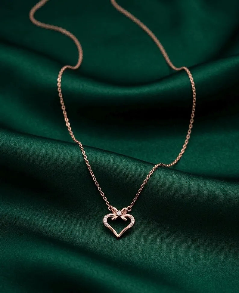 A delicate rose gold chain necklace with a double-heart pendant, displayed on draped dark green satin fabric.