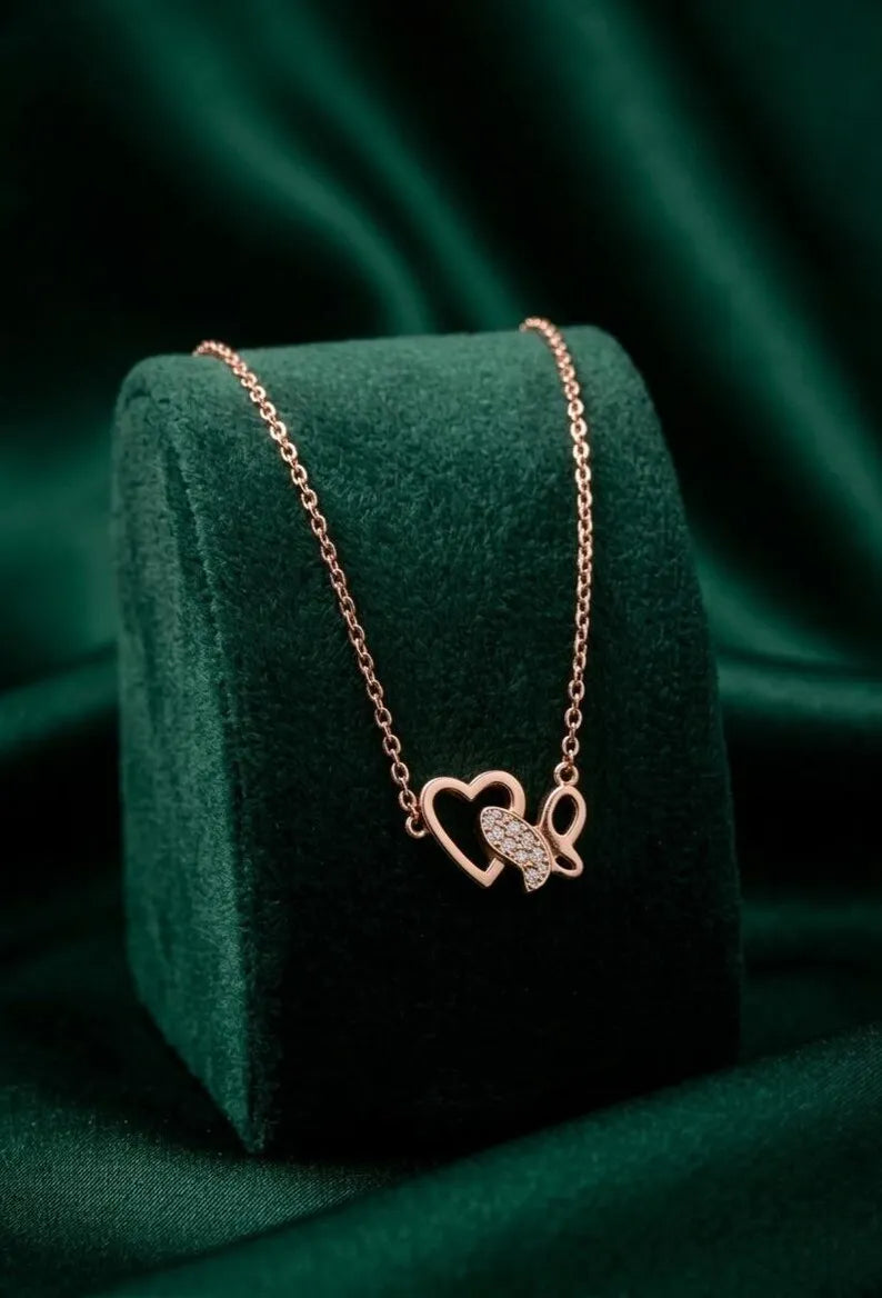 A rose gold necklace with a double-heart pendant, one of which is paved with small clear stones, displayed on a dark green velvet jewelry box against a matching green satin background.