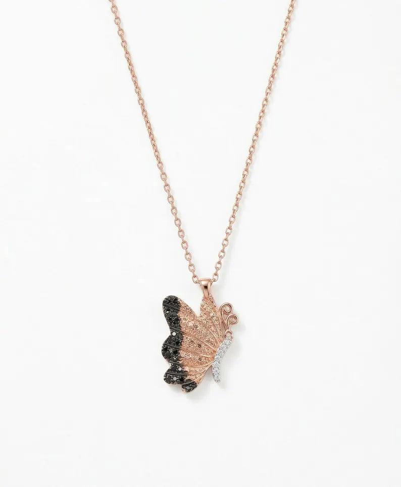 A delicate rose gold chain necklace featuring a butterfly pendant with one wing in sparkling black stones and the other in rose gold, accented with small clear crystals, shown against a plain white background.
