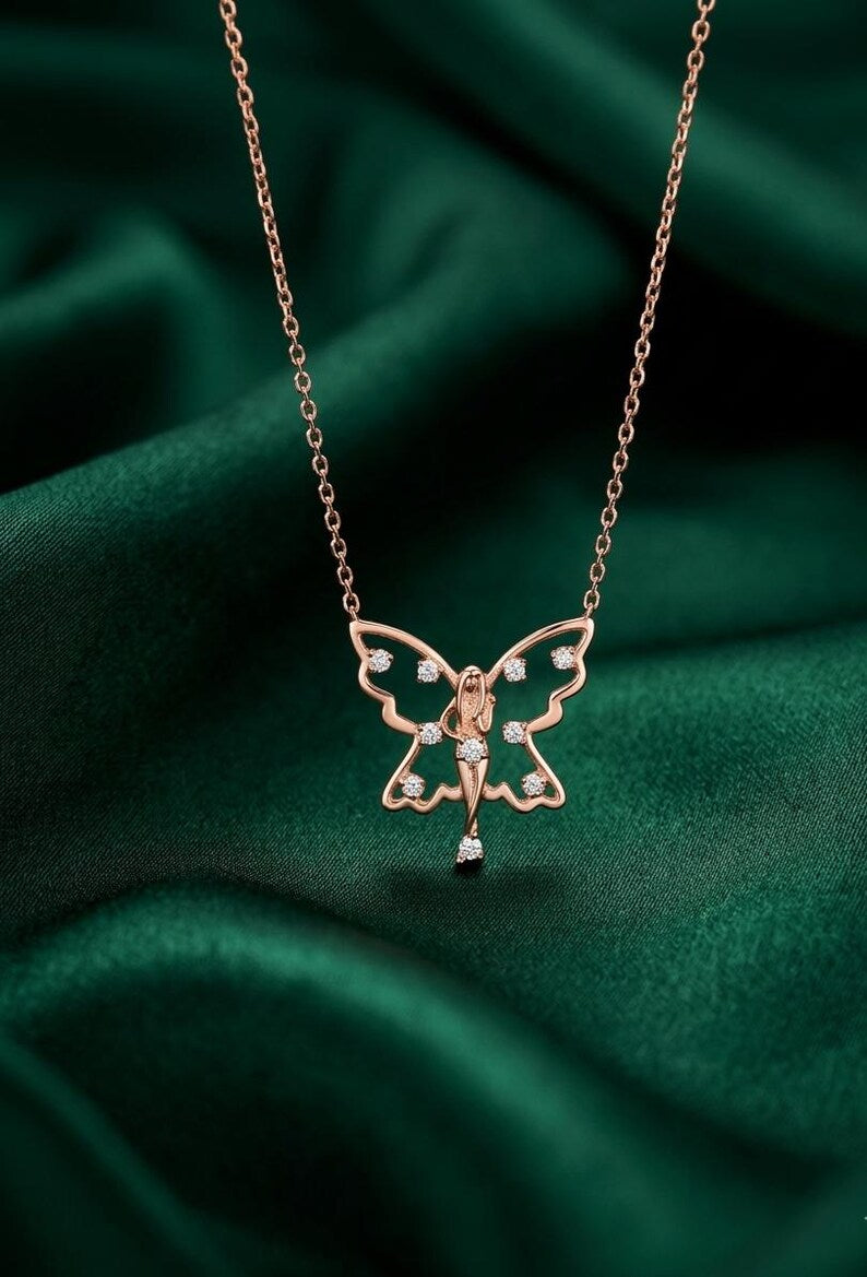 A rose gold butterfly pendant necklace with small clear gemstones, displayed on a dark green satin fabric background.