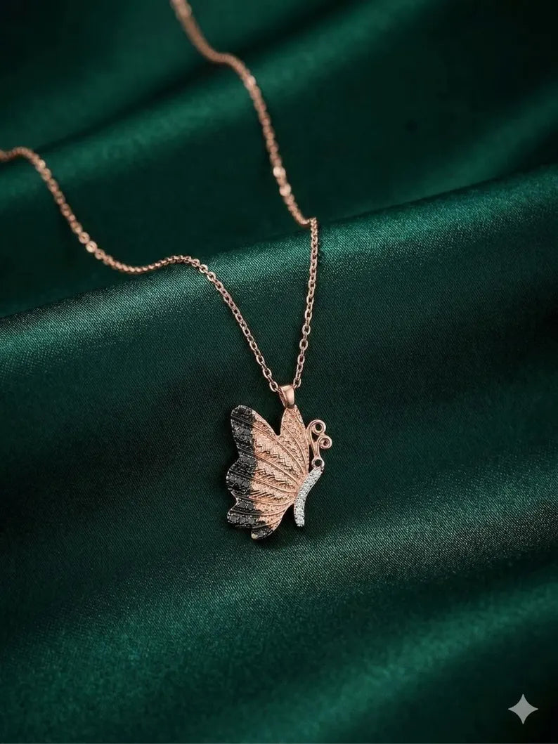 A delicate rose gold chain necklace with a butterfly pendant, displayed on draped dark green satin fabric.