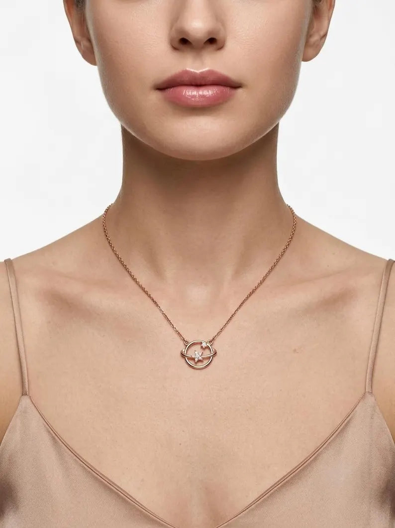 A close-up of a model wearing a delicate rose gold chain necklace with a small interlocking double-ring pendant, styled with a beige satin camisole against a clean white background.