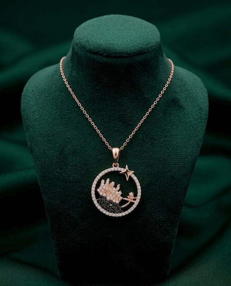 A rose gold pendant necklace featuring a circular design with a castle and star, displayed on a dark green velvet jewelry bust.