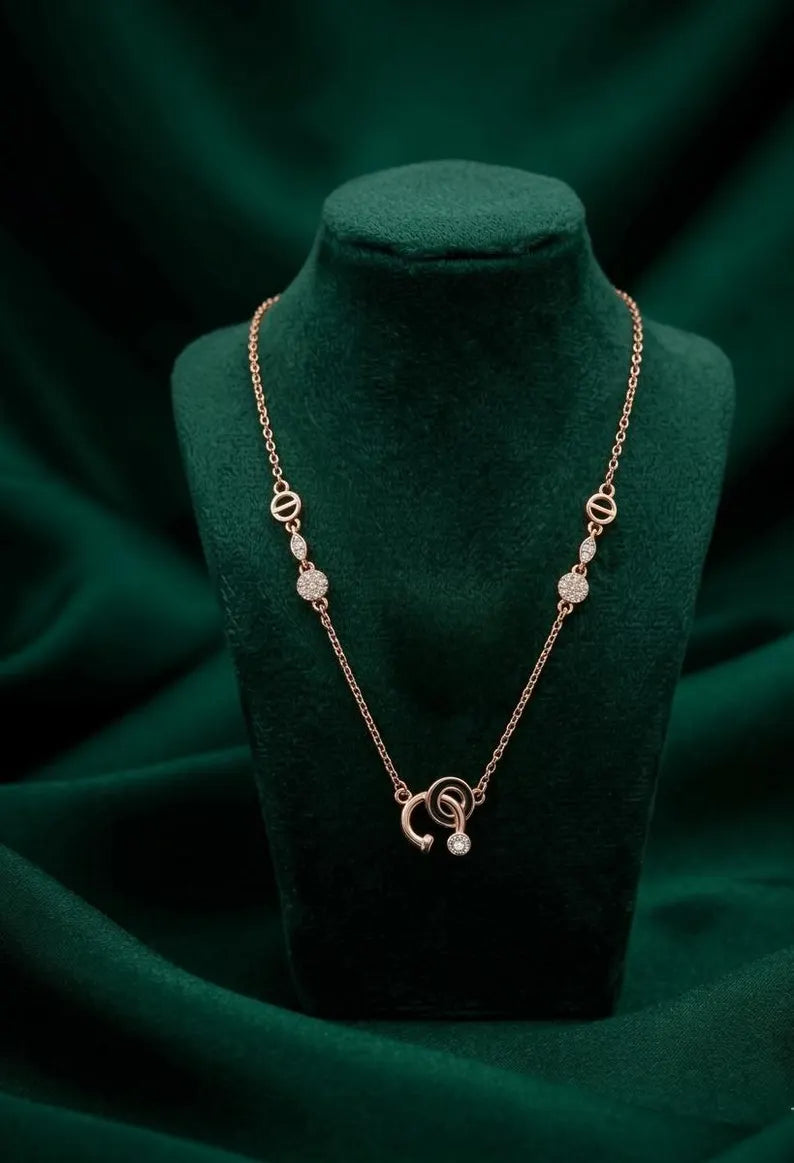 A delicate rose gold necklace with a crescent moon and pearl charm, displayed on a dark green velvet jewelry bust against a matching draped background.