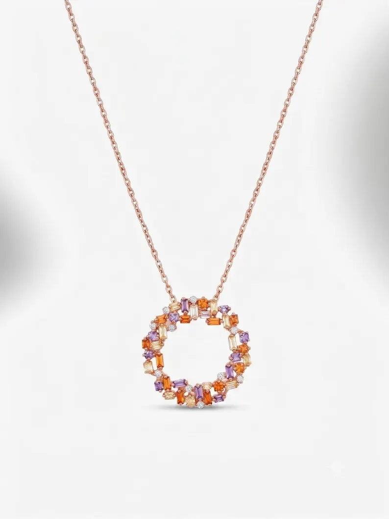 A delicate rose gold necklace featuring a circular pendant encrusted with small orange and purple gemstones, set against a clean white background.