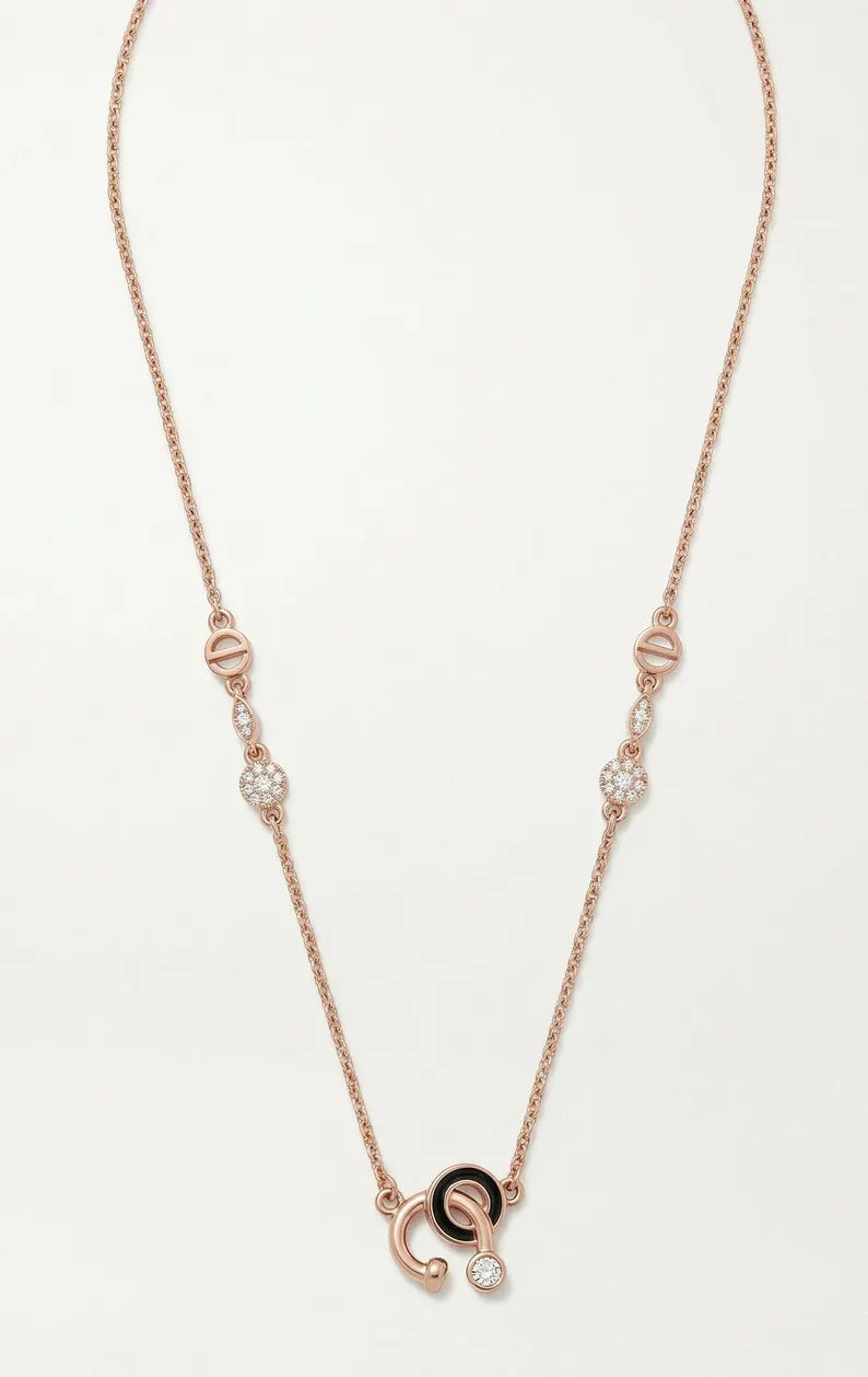 A delicate rose gold necklace featuring a double-C pendant with a black enamel center and small clear gemstone accents, displayed on a clean white background.