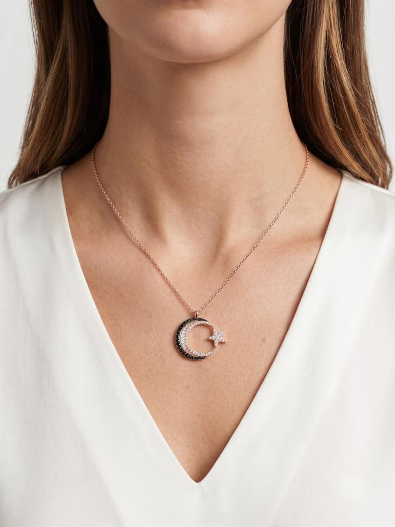 A close-up of a model wearing a delicate rose gold necklace with a crescent moon and star pendant, styled with a white V-neck top.