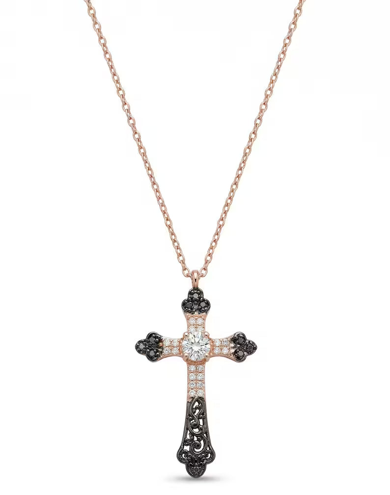 A rose gold cross pendant necklace with black and white gemstone accents, featuring a central clear round-cut stone, shown on a white background.