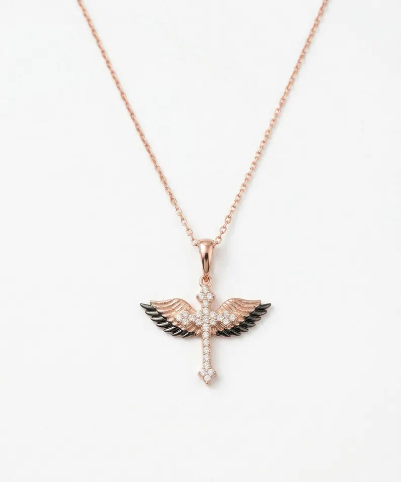 A rose gold winged cross pendant necklace with black enamel accents and clear crystal details, shown on a clean white background.