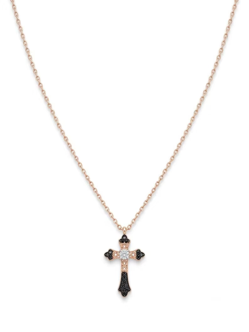 A delicate rose gold chain necklace with a cross pendant featuring black and clear stones, displayed against a solid white background.