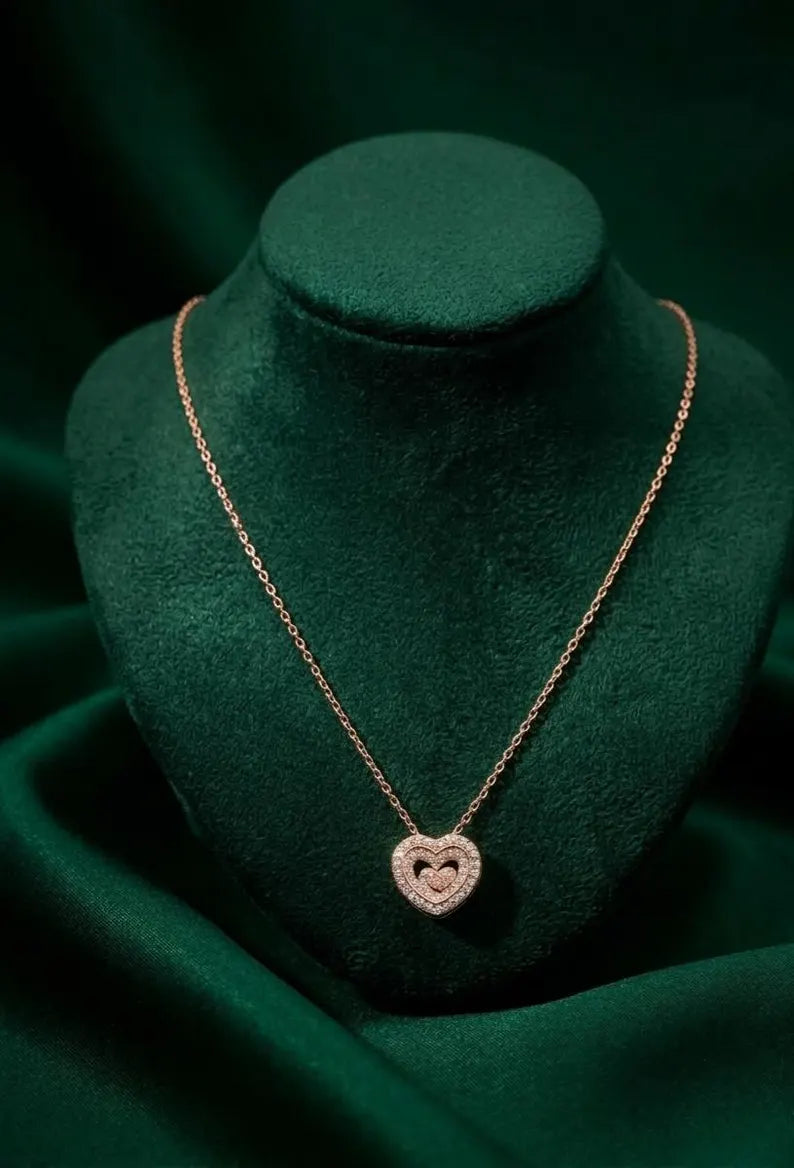 A rose gold heart pendant necklace displayed on a dark green velvet jewelry bust against a matching dark green fabric background.