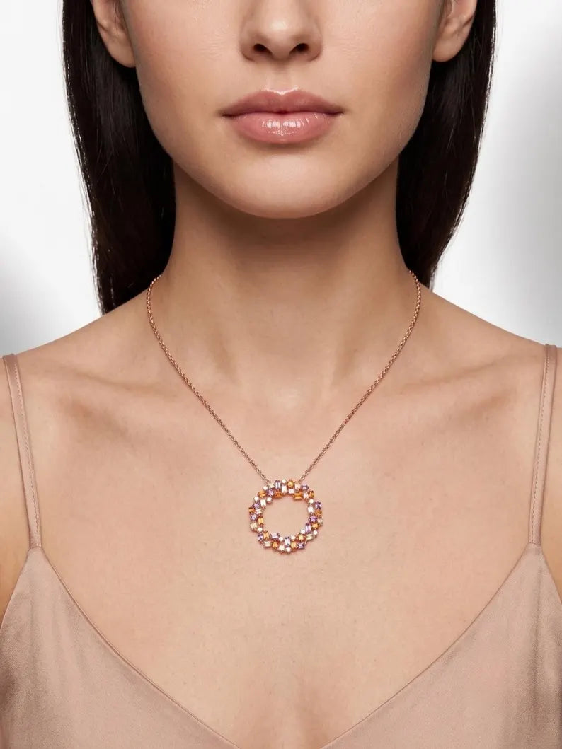 A close-up of a model wearing a delicate rose gold necklace with a circular pendant adorned with small, iridescent, multi-colored rhinestones.
