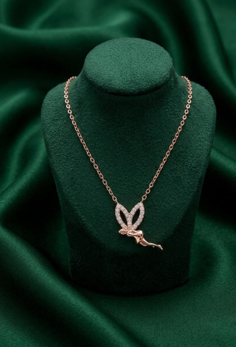 A rose gold pendant necklace featuring a stylized butterfly with pavé-set clear stones, displayed on a dark green velvet jewelry bust against a draped green satin background.