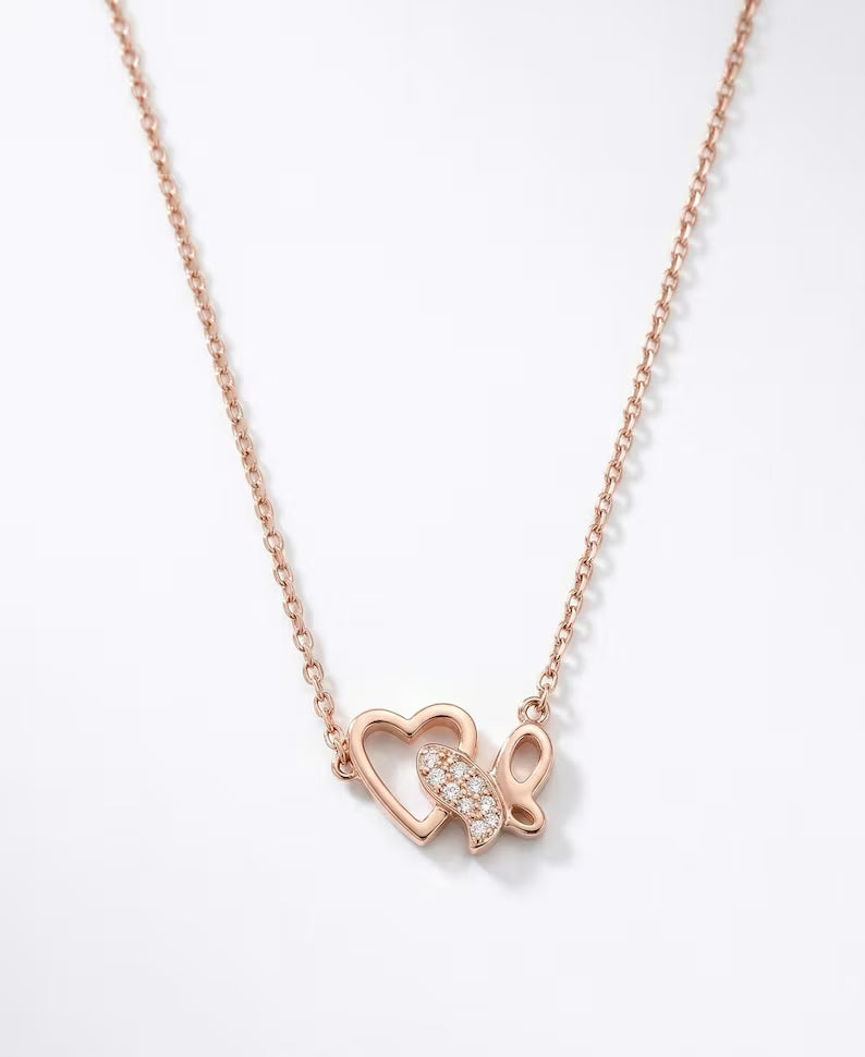 A rose gold necklace featuring a delicate chain and a pendant composed of two interlocking open hearts, one of which is adorned with a small cluster of clear pavé stones, set against a clean white background.