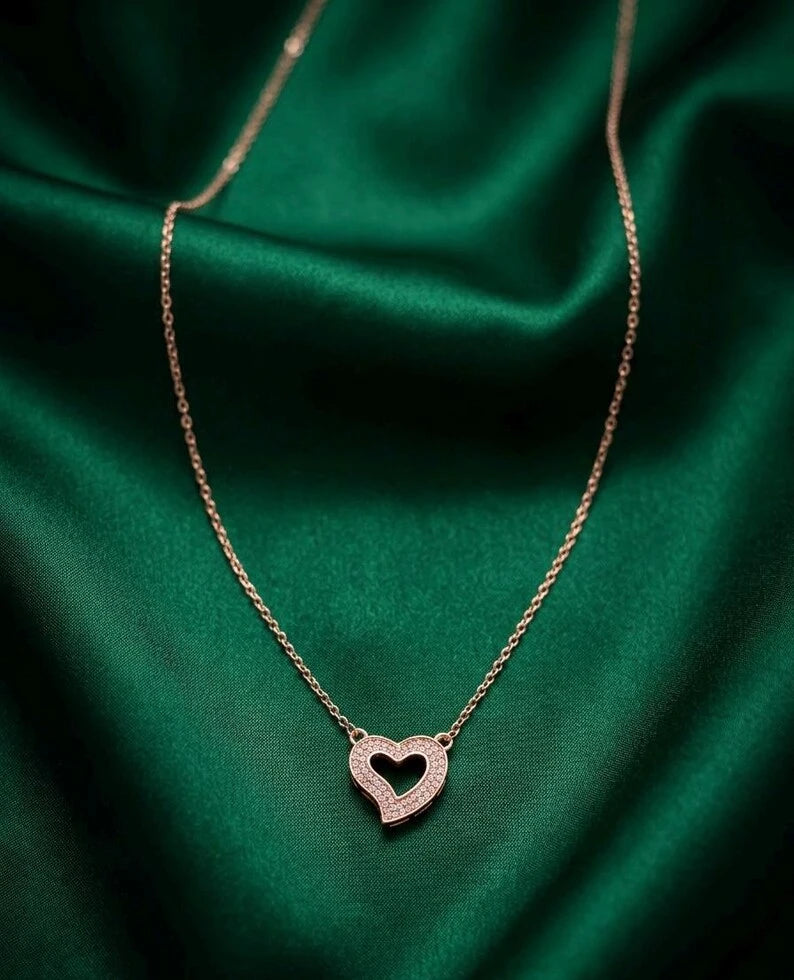 A delicate rose gold chain necklace with a double-heart pendant, displayed on a draped emerald green satin fabric.