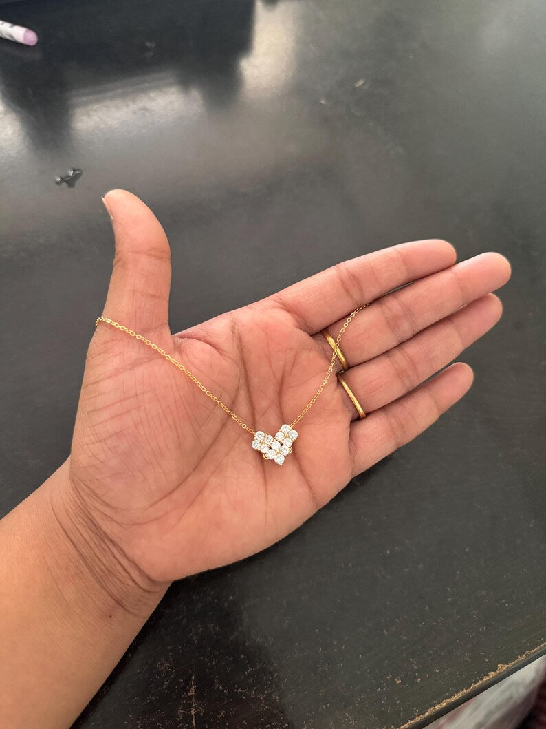 A gold chain necklace with a small cluster of clear stones pendant, held in a person's open palm over a dark tabletop.