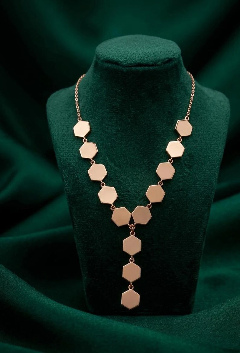 A rose gold geometric necklace with hexagonal links displayed on a dark green velvet jewelry bust.