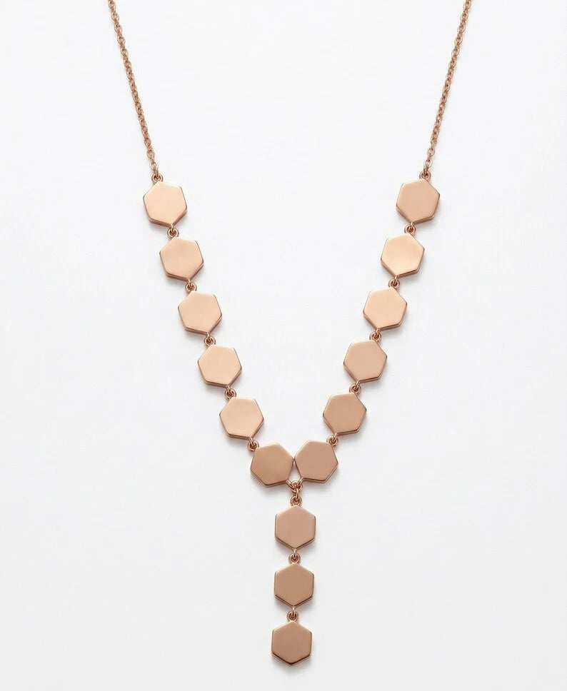A rose gold Y-necklace featuring a series of flat hexagonal discs connected by small beads, suspended from a delicate chain against a plain white background.