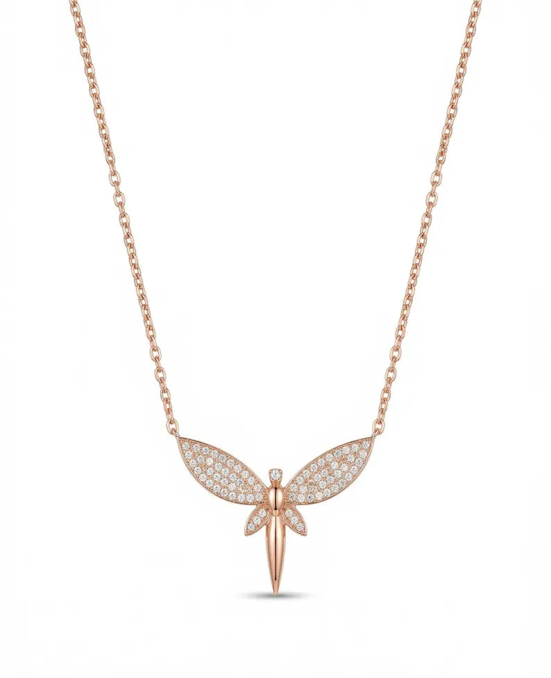 A rose gold dragonfly pendant necklace with pavé-set clear stones on its wings, suspended from a delicate rose gold chain against a solid white background.