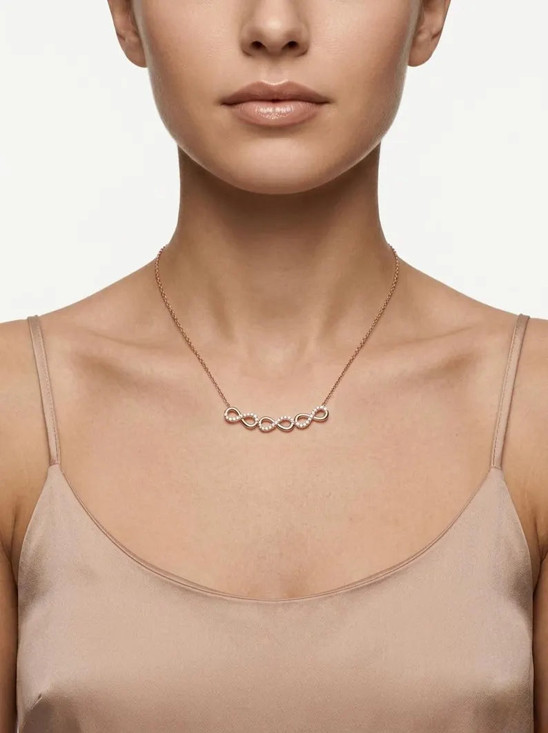 A close-up of a model wearing a delicate rose gold necklace with a row of small, connected oval links, styled with a beige satin camisole top against a clean white background.