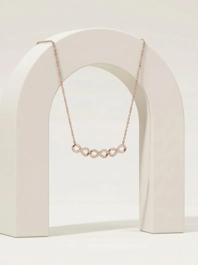 A delicate rose gold necklace with a curved bar of small linked oval charms, displayed draped over a white arched stand against a clean white background.