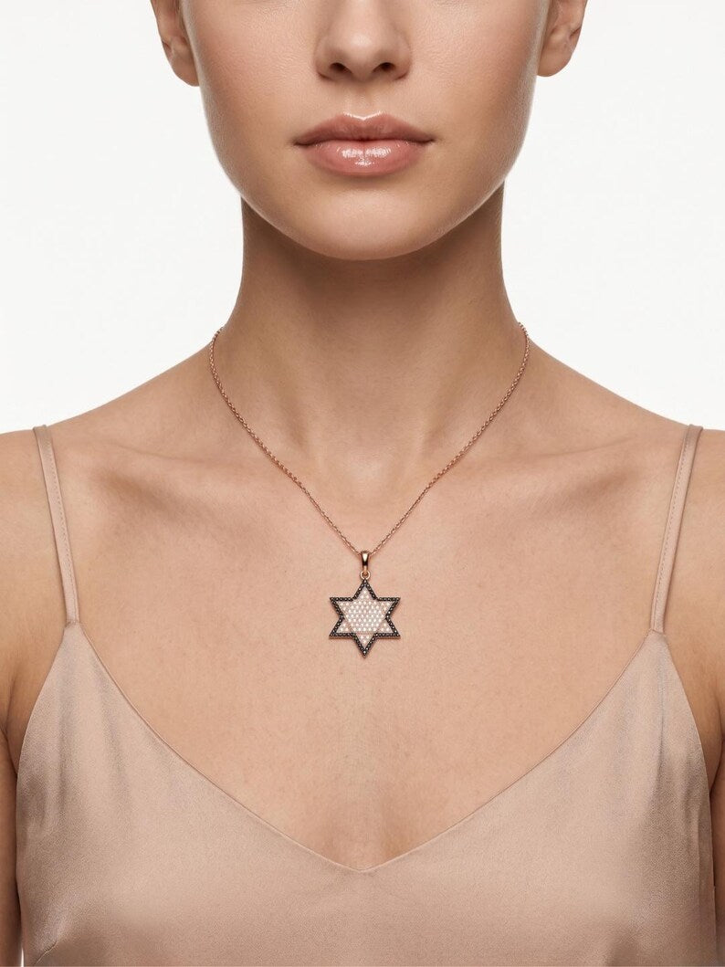 A close-up of a model wearing a delicate rose gold chain necklace with a Star of David pendant paved with clear crystals, set against a clean white background.