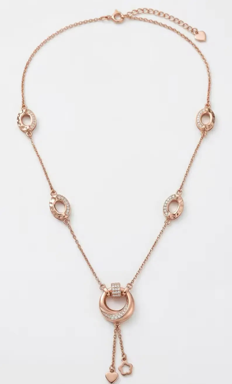 A rose gold layered statement necklace with zircon circle pendant featuring a central double-ring pendant with small clear stones, flanked by three matching circular ring charms on a delicate chain, displayed on a clean white background.