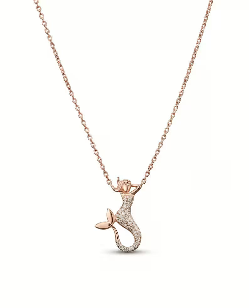 A rose gold mermaid pendant necklace on a delicate chain, featuring a mermaid design paved with small clear stones on her tail, set against a plain white background.