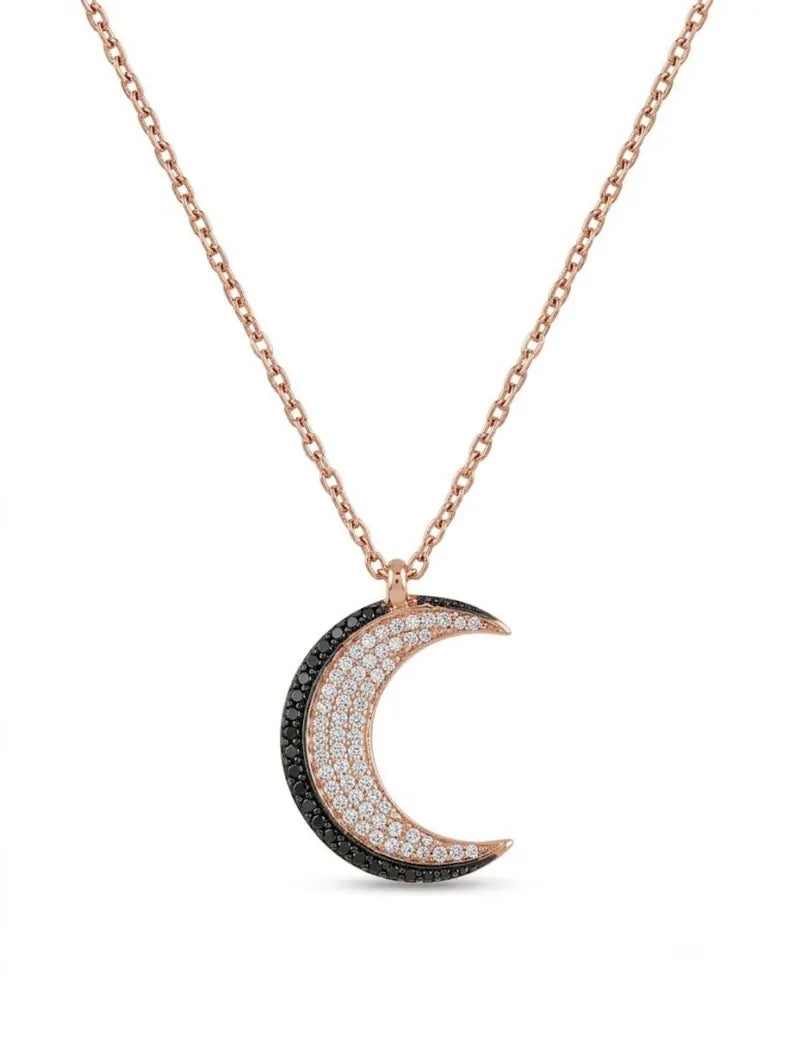 A rose gold crescent moon pendant necklace on a delicate chain, featuring a black pavé-set edge and a white pavé-set center, shown against a plain white background.