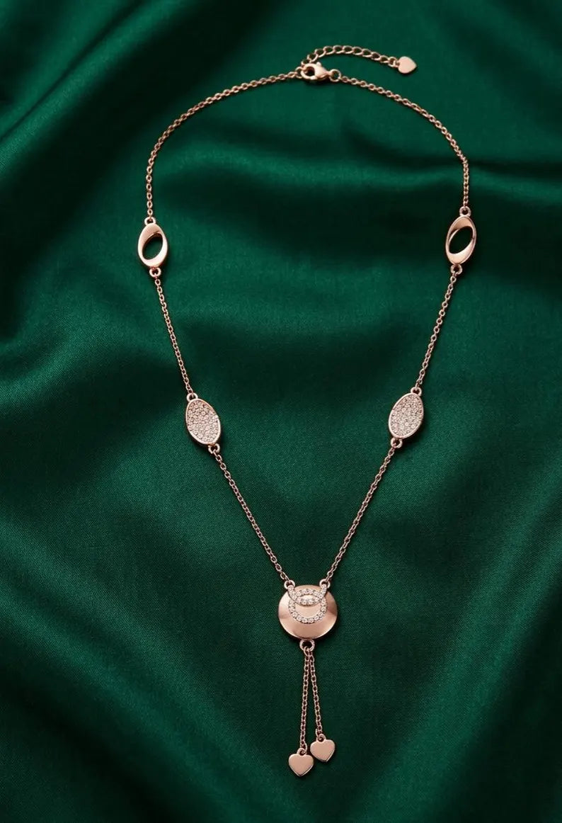 A rose gold chain necklace with heart pendant, 925 sterling silver with multiple oval and oval-link charms, laid out on a draped dark green satin fabric background.