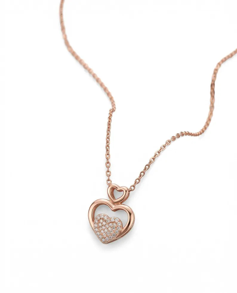 A rose gold necklace with a heart-shaped pendant, featuring a pavé-set heart inside an open heart frame, on a clean white background.