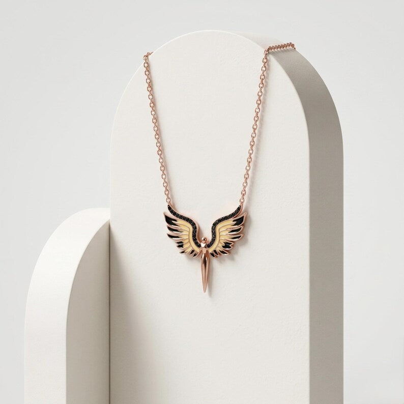 A rose gold necklace with a winged pendant displayed on a white arched stand against a light gray background.