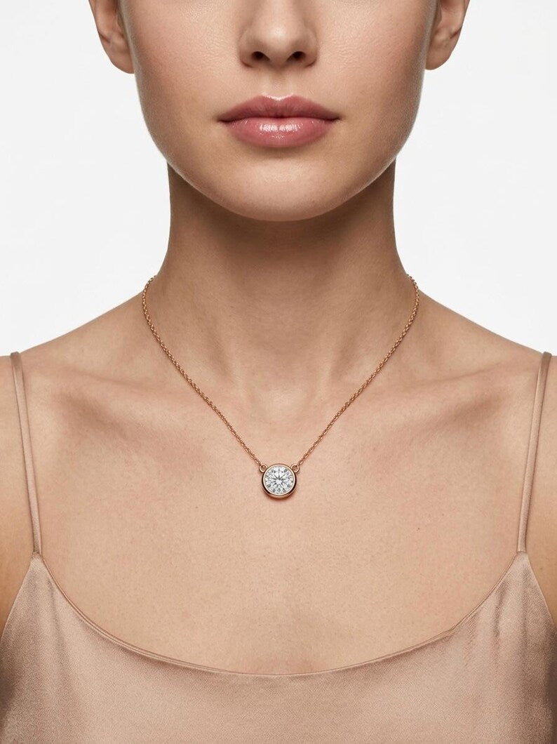 A close-up of a model wearing a delicate rose gold chain necklace with a round, clear gemstone pendant.