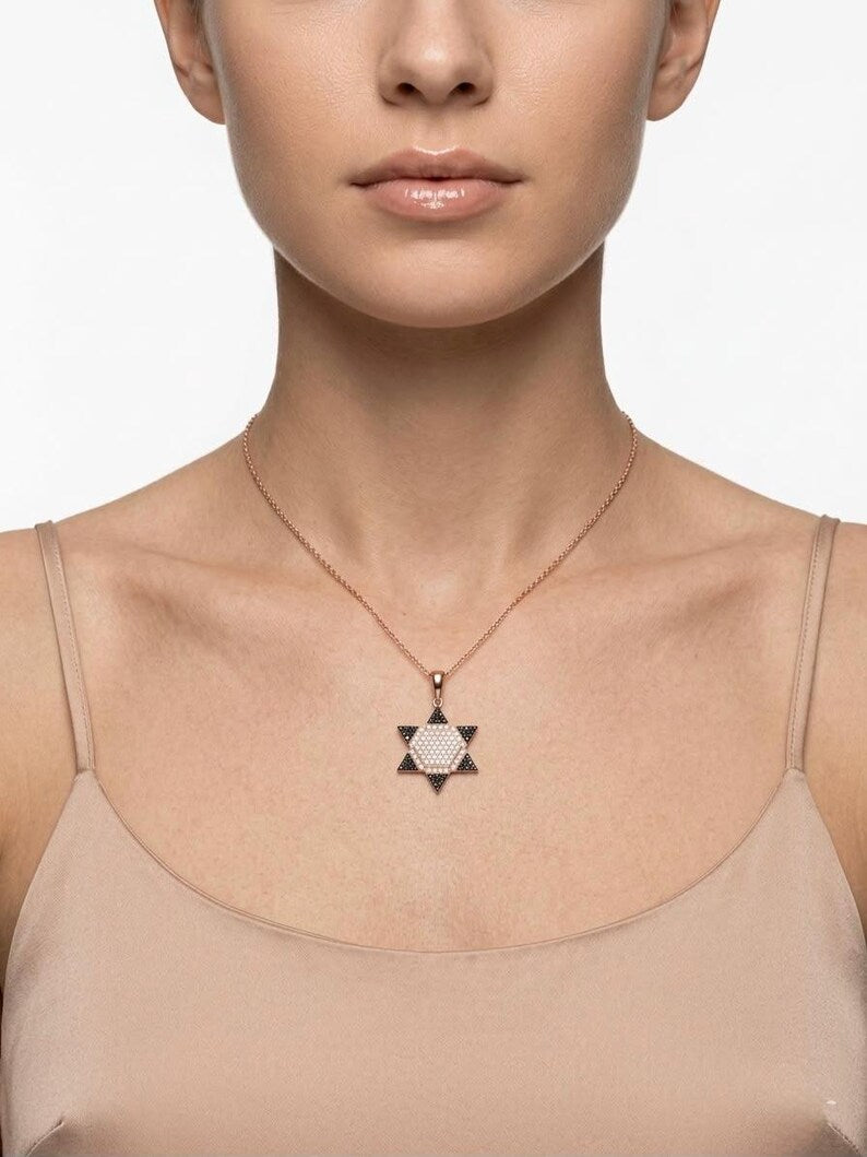 A close-up of a model wearing a rose gold necklace with a Star of David pendant featuring a textured white center.