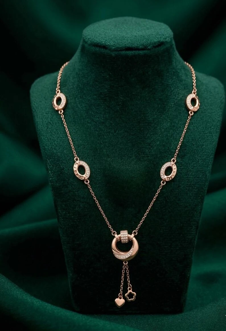 A rose gold necklace with circular ring motifs and a central ring pendant, displayed on a dark green velvet jewelry bust.