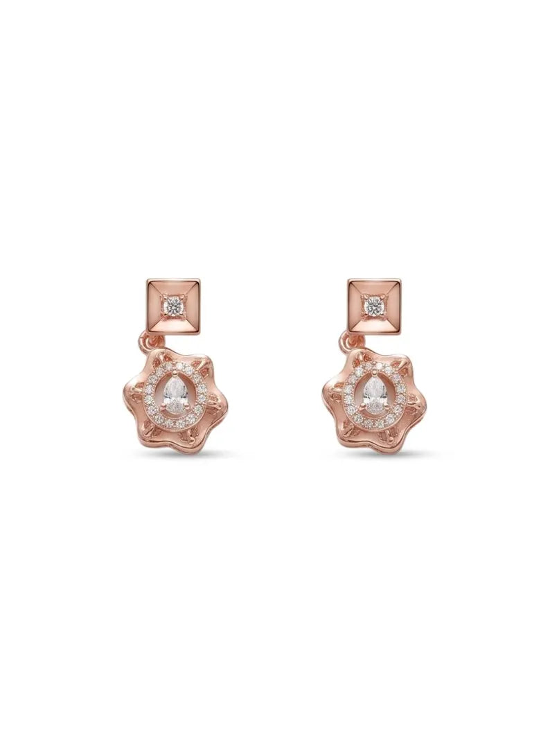 A pair of rose gold dangle earrings featuring a square post with a small clear gemstone and a flower-shaped drop with a larger oval clear gemstone surrounded by small stones, set against a plain white background.