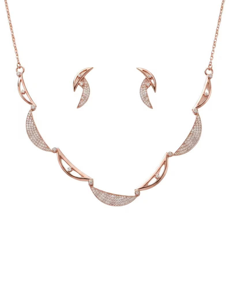 Rose gold jewelry set featuring a crescent moon pendant necklace and matching crescent moon stud earrings, both adorned with pavé-set clear stones on a white background.