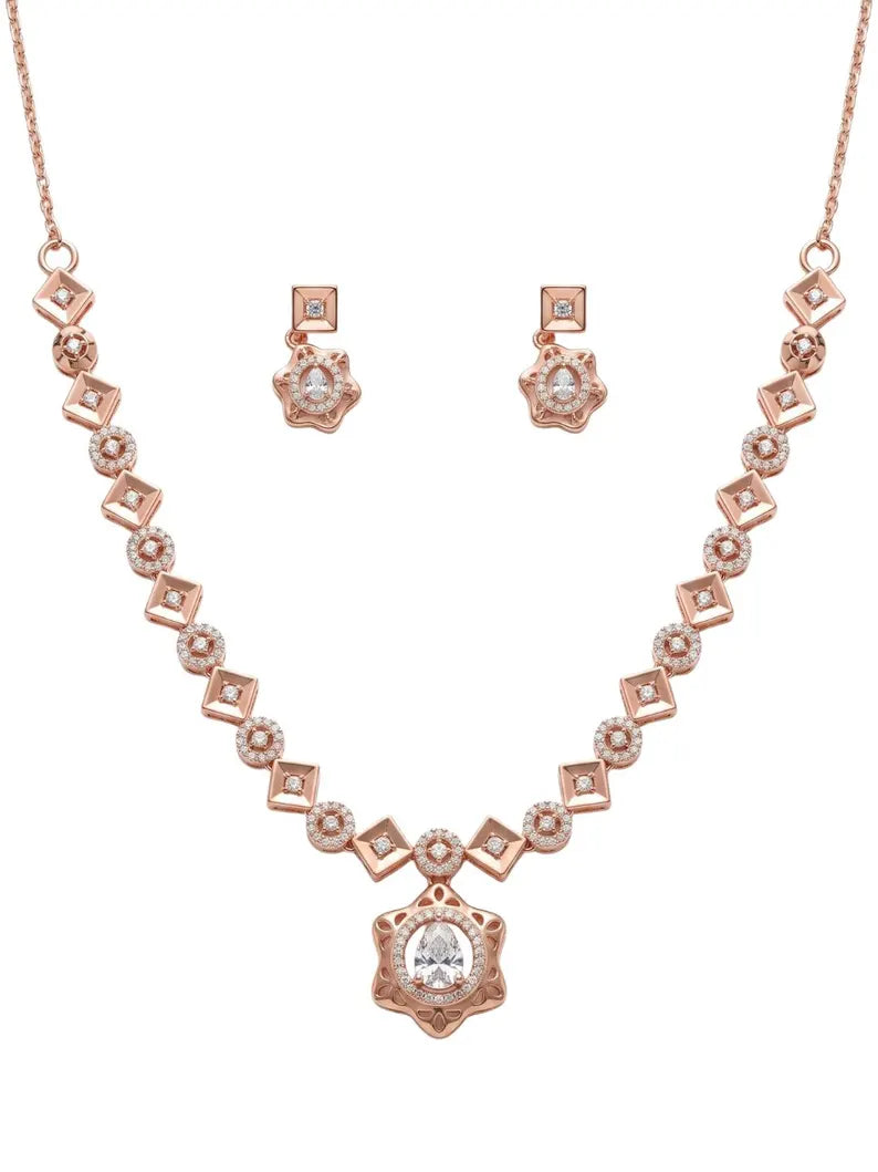 Rose gold jewelry set featuring a necklace with a central floral pendant, matching drop earrings, and a chain, all adorned with clear gemstones on a plain white background.