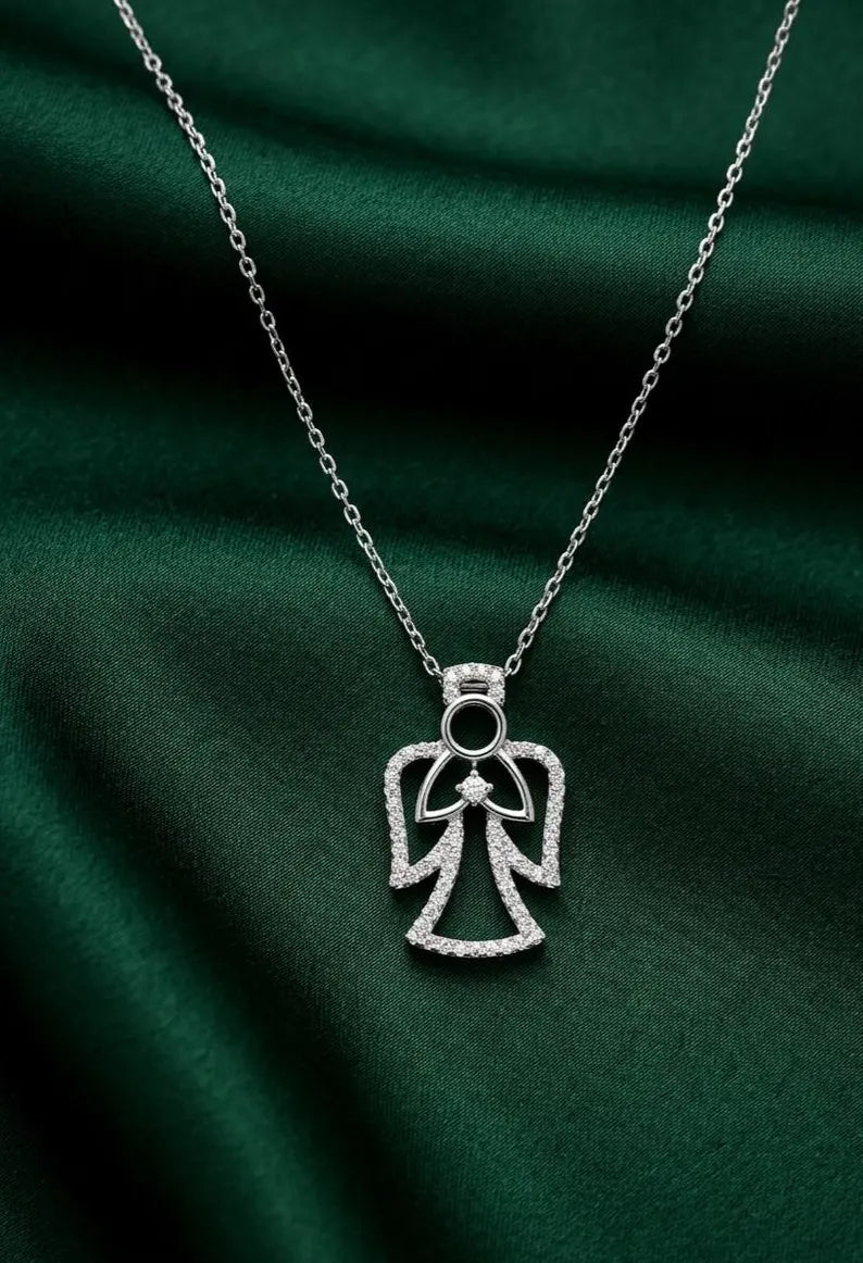 A silver angel pendant necklace adorned with small clear stones, displayed on a draped dark green satin fabric background.