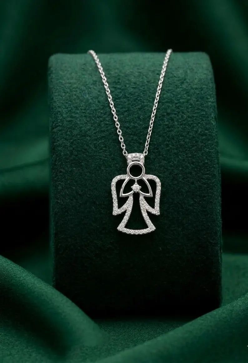 A silver angel pendant necklace with a small black center stone, displayed on a dark green velvet jewelry stand.