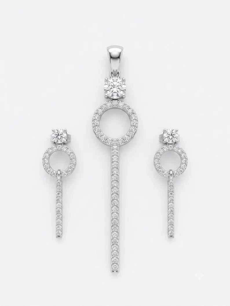A jewelry set featuring a pendant and two matching drop earrings in a silver-tone metal, each adorned with clear gemstones, displayed on a clean white background.