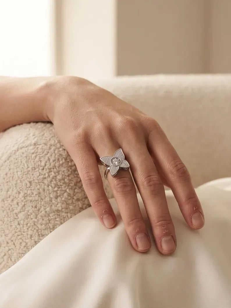 Hand resting on cream fabric wearing a sterling silver flower ring with pave petals and a round CZ center