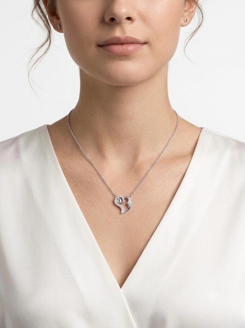 A close-up of a woman wearing a delicate silver pendant necklace with a crescent moon and heart design, paired with a white V-neck top against a clean white background.