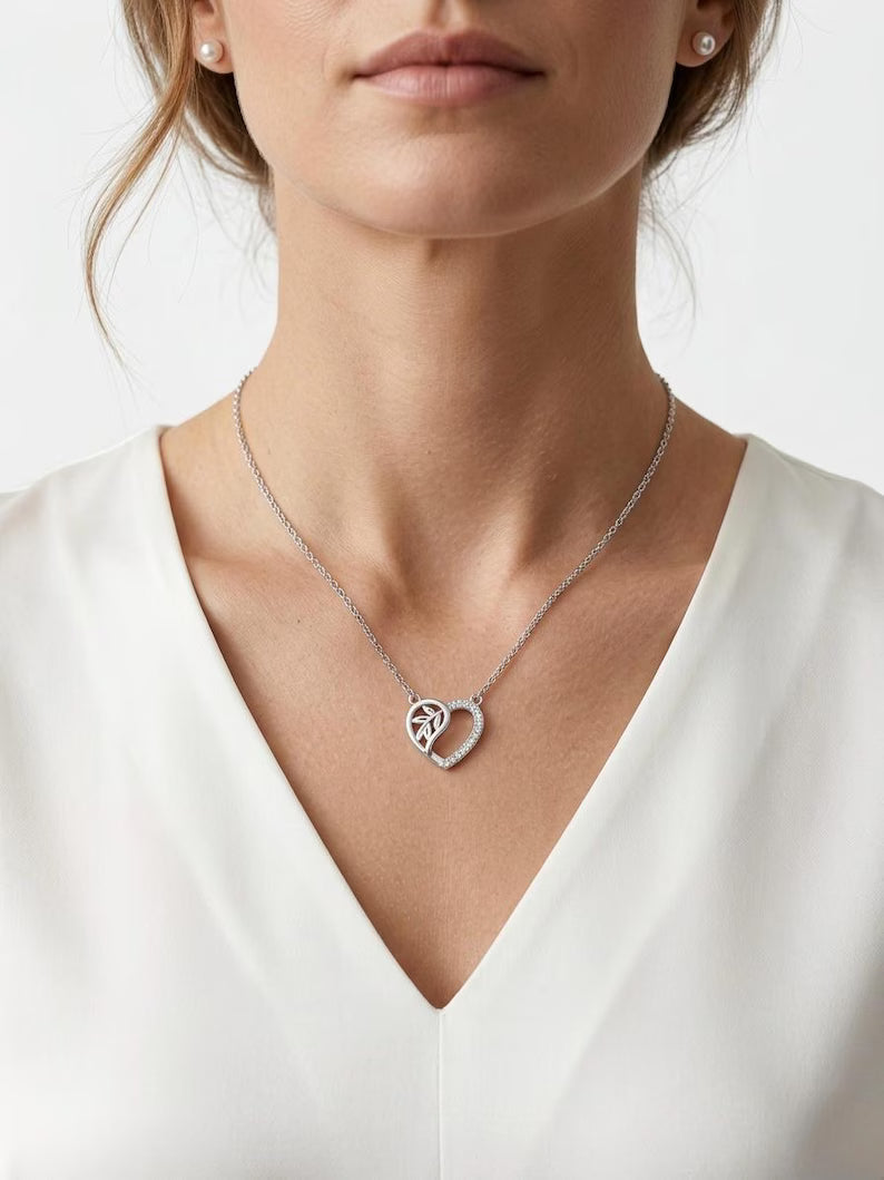 A close-up of a woman wearing a delicate silver heart-shaped pendant necklace with a pavé center, styled with a white V-neck top.